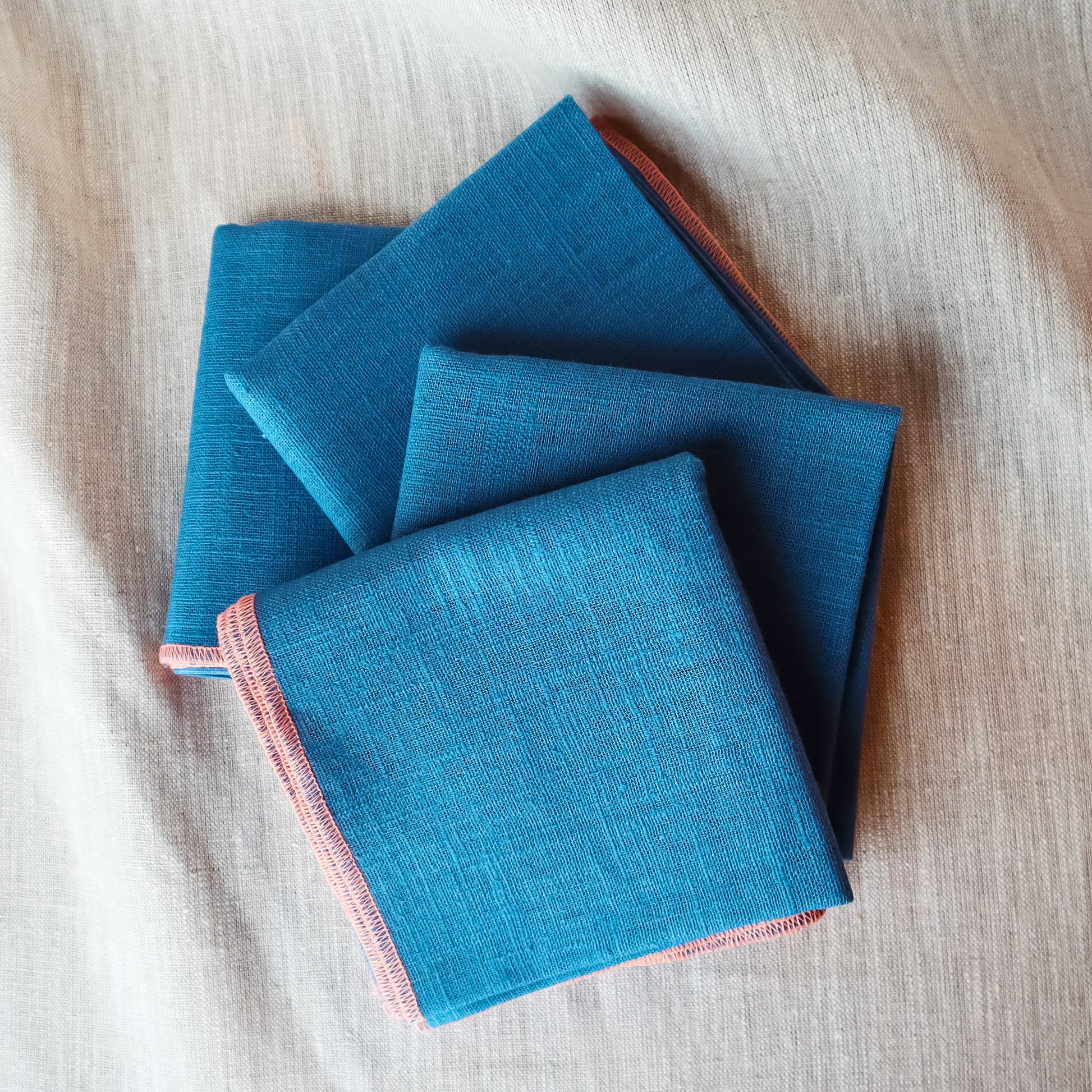 Three blue fabric napkins stacked on a beige surface