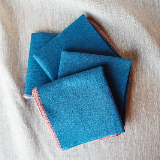 Three blue fabric napkins stacked on a beige surface